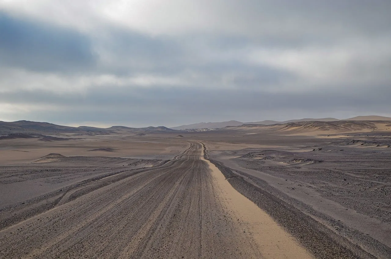 namibia, desert road, gravel road, tire tracks, clouded sky, sand landscape, rock landscape, lonliness, long-distance travel, wilderness, expanse, adventure, offroad, nature, steppe, dry landscape, horizon, isolation, vehicle lane, barren landscape. Water, fuel, and navigation: the real packing list for slow road travel